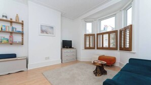 En stue med sofa, sofabord, fjernsyn, reol og et vindue med skodder.