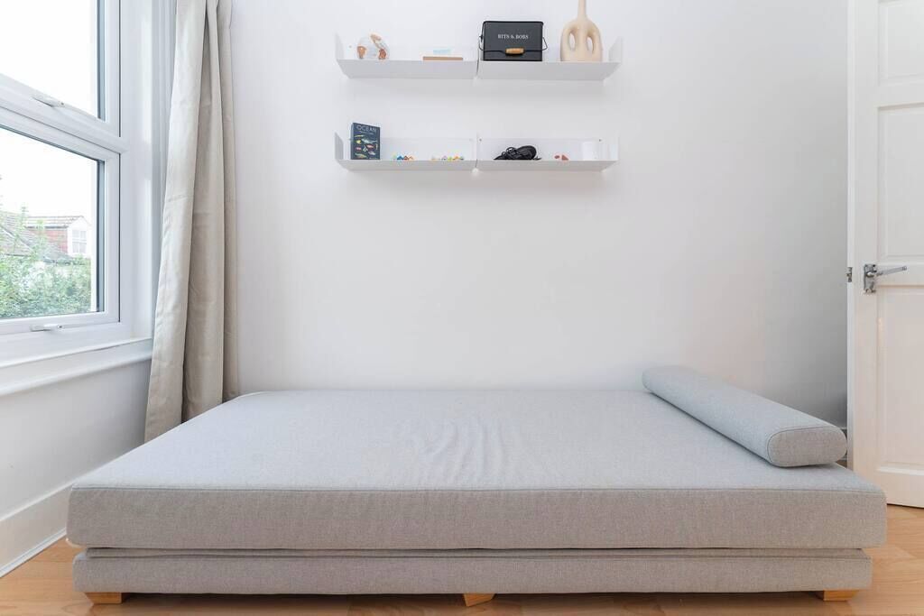 A minimalist room with a single bed, white shelving units, and a window with curtains.
