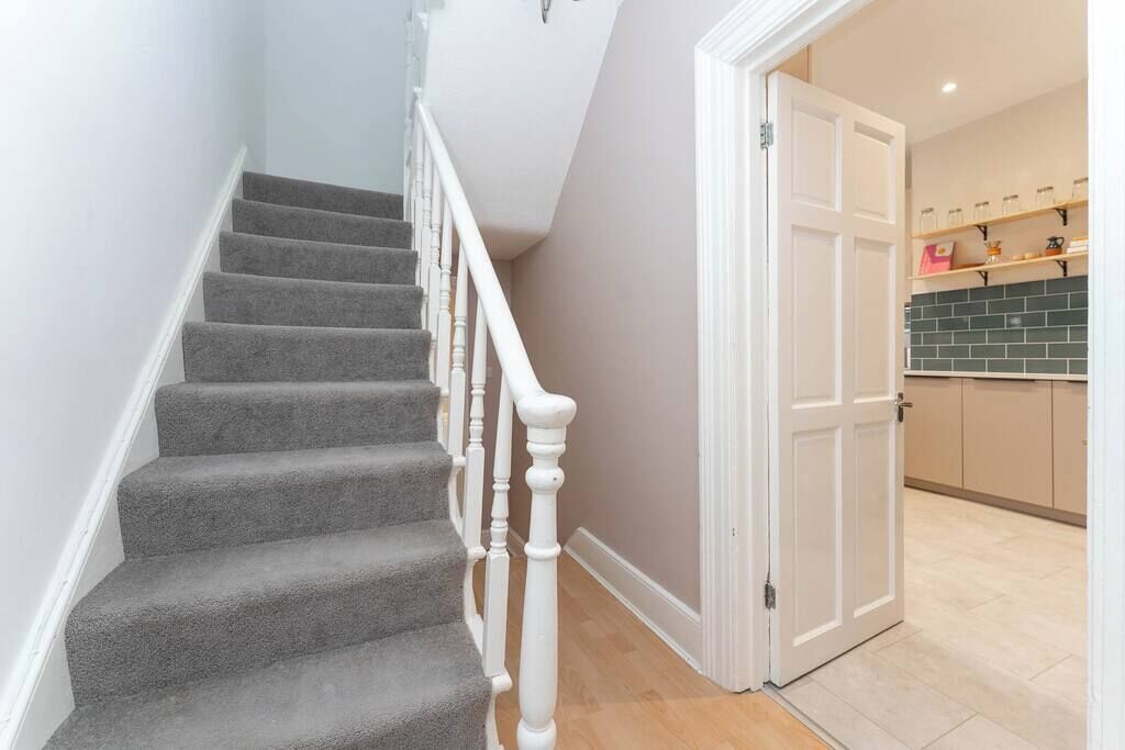 Eine Treppe mit Teppichstufen und weißen Wangen, die zu einem Raum mit Fliesenrückwand und Holzausbau führt.