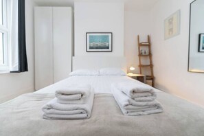 Una cama bien hecha con toallas dobladas, una mesita de noche con una lámpara y un cuadro en la pared.
