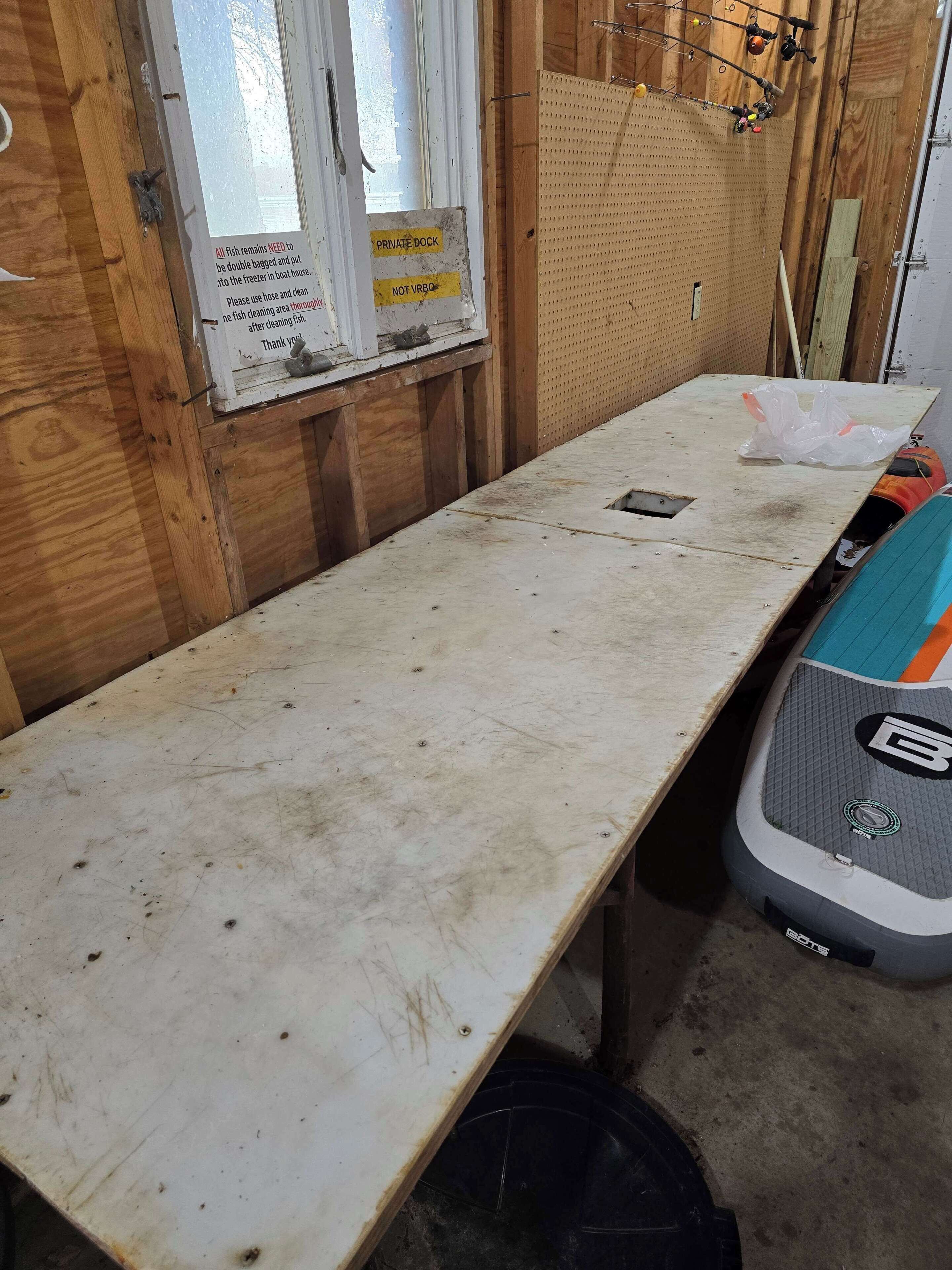 Un banco de trabajo de madera con un cartel sobre manipulación de pescado, un tablero de corcho y una herramienta eléctrica.