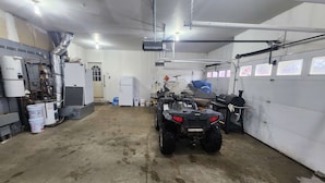 A garage with a dirt floor, a white refrigerator, a water heater, and a black ATV.