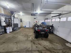 A garage with a dirt floor, a white refrigerator, a water heater, and a black ATV. - Luxury Family 5BR Lakefront private boat launch (Big Stone City)