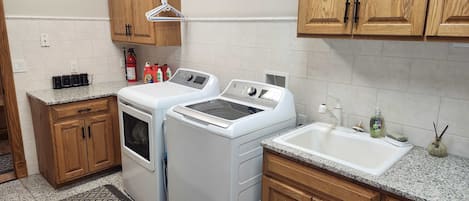 Un área de lavandería con dos lavadoras, un tendedero, armarios de madera y un lavabo.