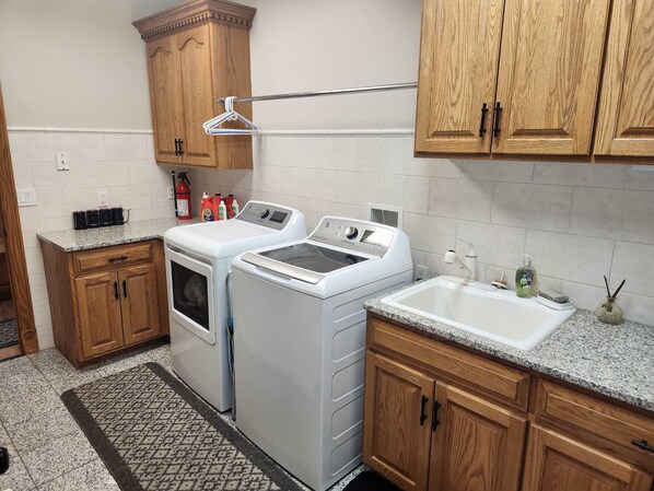 A laundry area with two washing machines, a drying rack, wooden cabinets, and a sink.
