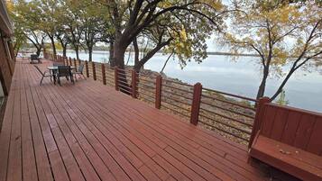 A wooden deck with a railing overlooking a body of water, featuring benches and tables.