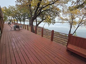 A wooden deck with a railing overlooking a body of water, featuring benches and tables.