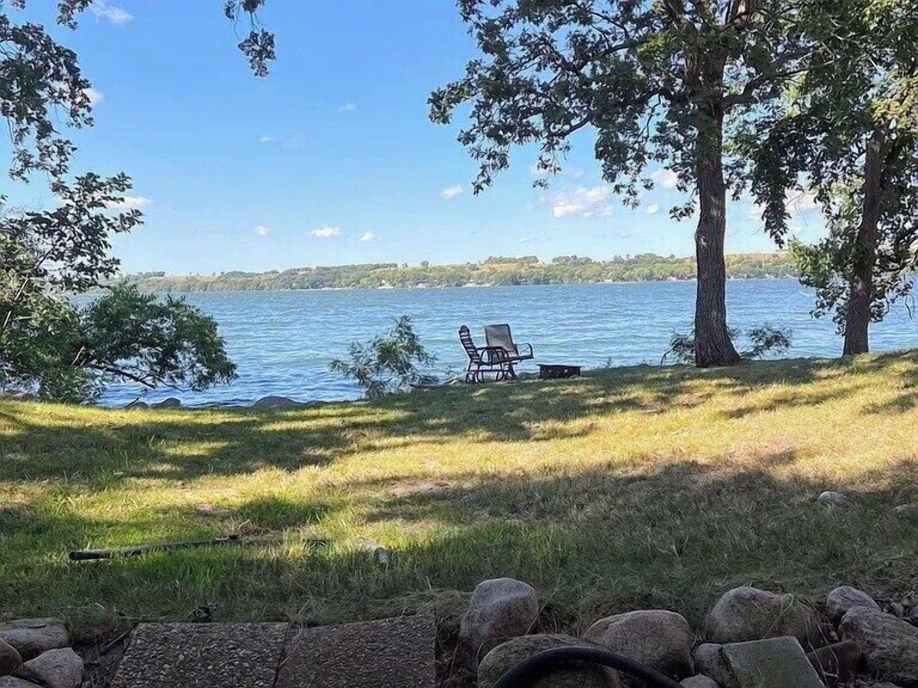 Vista sul lago con un prato, due sedie e un muro in pietra.