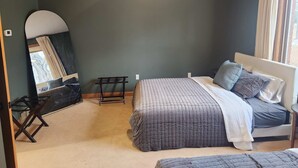 A bedroom with a bed, a bedside table, a chair, a mirror, and a window with curtains.