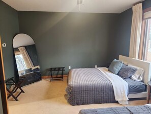 A bedroom with a bed, a bedside table, a chair, a mirror, and a window with curtains.