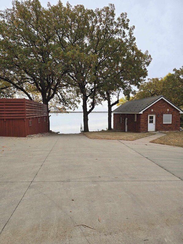 A building with a brick exterior, a small attached garage, and a concrete driveway leading to a wooden dock.
