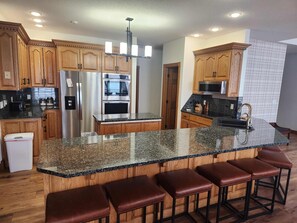 Una cocina moderna con armarios de madera, encimeras de granito, electrodomésticos de acero inoxidable y una zona de bar con taburetes.