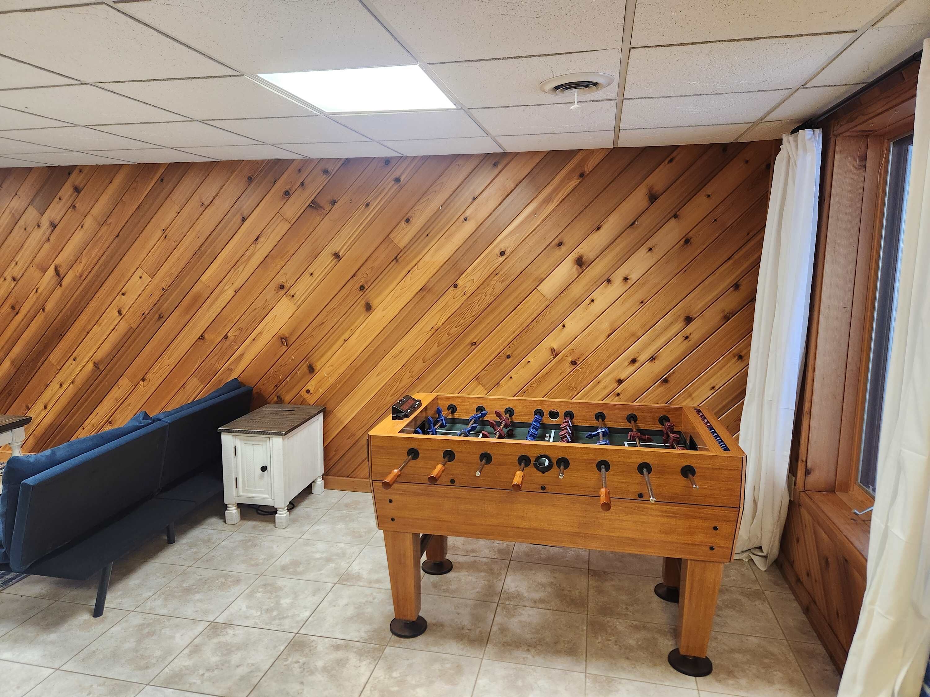 A room with a wooden sloped ceiling, a foosball table, a sofa, and a cabinet.