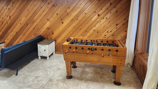 Um quarto com teto inclinado de madeira, mesa de futebol, sofá e um armário.
