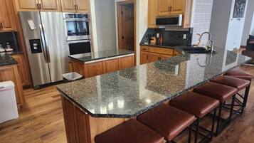 A kitchen with wooden cabinets, stainless steel appliances, a granite countertop, and bar stools.