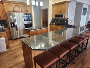 A kitchen with wooden cabinets, stainless steel appliances, a granite countertop, and bar stools.