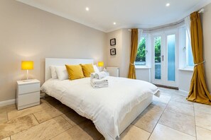 Une chambre avec un grand lit, deux tables de chevet, une fenêtre avec des rideaux et une vue sur la verdure.