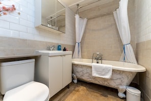 Une salle de bain avec une baignoire en marbre, des toilettes blanches et un lavabo équipé de produits de toilette.