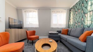 A modern living room with a grey sofa, orange armchairs, a wooden coffee table, and a TV on a wooden cabinet. - Host & Stay | Portland Apartment (Brighton and Hove)
