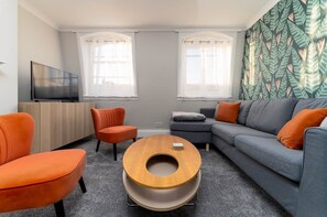 A modern living room with a grey sofa, orange armchairs, a wooden coffee table, and a TV on a wooden cabinet.
