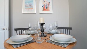 A dining table set with white plates, glasses, and a candle centerpiece. Two framed pictures hang on the wall above. - Host & Stay | Portland Apartment (Brighton and Hove)