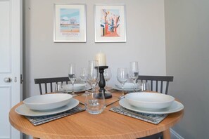 A dining table set with white plates, glasses, and a candle centerpiece. Two framed pictures hang on the wall above. - Host & Stay | Portland Apartment (Brighton and Hove)