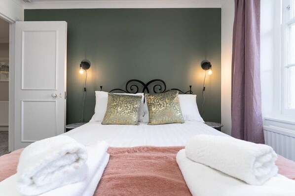 A neatly made bed with two pillows, a pink throw blanket, and two towels on either side.