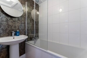 Ein Badezimmer mit einem weißen Waschtisch, einer Duschkabine aus Glas und Wandtapete mit Muster.