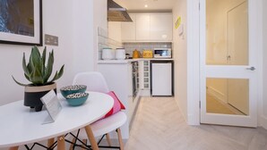 Una cocina compacta con armarios blancos, un microondas y un refrigerador pequeño.