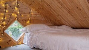 A cozy attic bedroom with a sloped ceiling, a large window, and string lights.