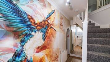 Um corredor com um grande mural de beija-flor, uma escada e uma porta branca.