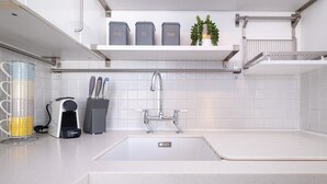 A modern kitchen with a white countertop, a sink, and a coffee machine. There are three grey storage containers labeled coffee, tea, and sugar on a shelf above the sink. - Host & Stay | Guildford Apartment (Brighton and Hove)