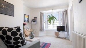 A modern living room with a sofa, a TV, a window with curtains, and a plant. - Host & Stay | Guildford Apartment (Brighton and Hove)