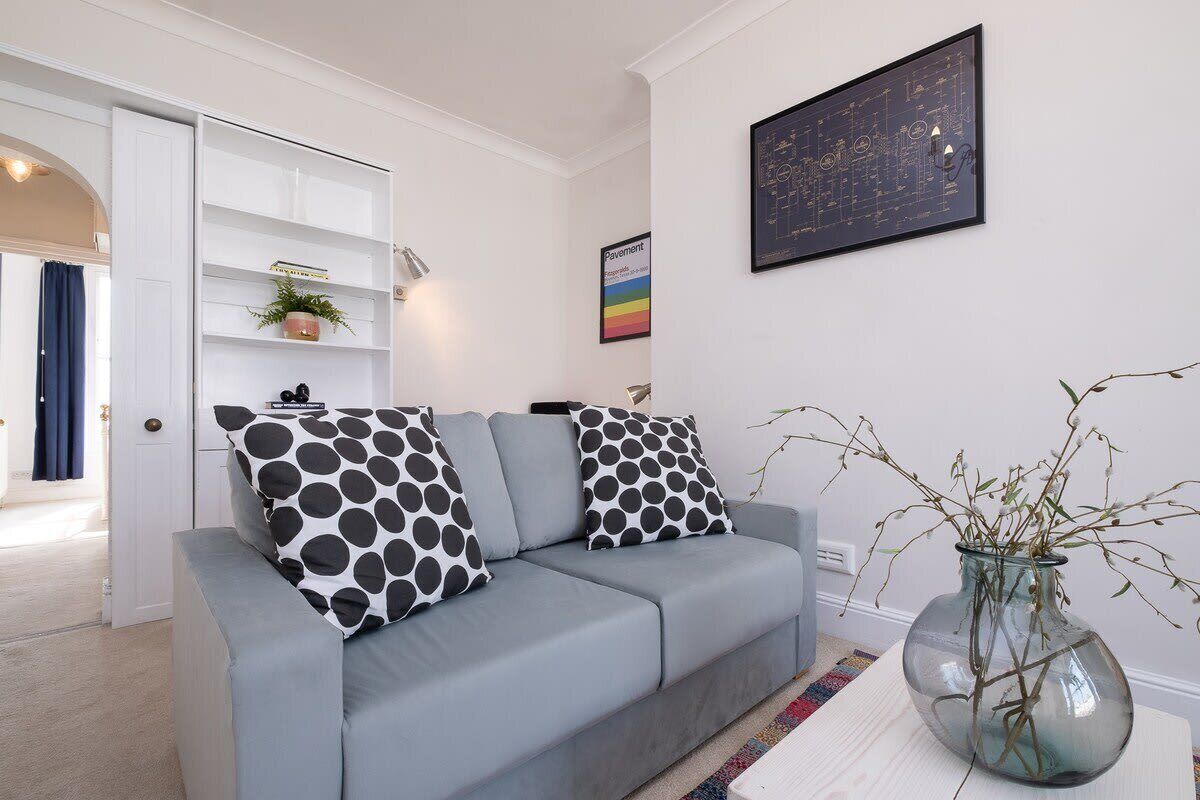 A modern living room with a grey sofa, black and white polka dot cushions, a glass vase with branches, and a framed map on the wall.