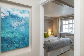 A bedroom with a bed, a nightstand, a window with curtains, and a painting on the wall. - Host & Stay | Sillwood Seafront (Brighton and Hove)