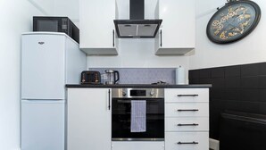 A compact kitchen with a white refrigerator, a microwave, an oven, and a clock on the wall. - Host & Stay | Preston Park Apartment (Brighton and Hove)