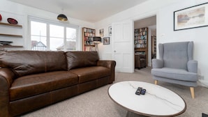 A living room with a brown leather sofa, a grey armchair, a white marble coffee table, and a bookshelf filled with books. - Host & Stay | Preston Park Apartment (Brighton and Hove)