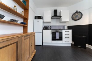 Een compacte keuken met witte kastjes, een zwarte koelkast, een magnetron, een koffiezetapparaat en een klok aan de muur.