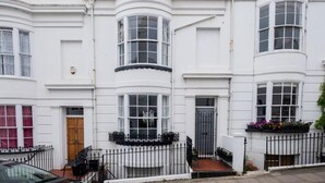 A row of white townhouses with bay windows, a wooden door, and a black metal fence. - Host & Stay | Montpelier Colours (Brighton and Hove)