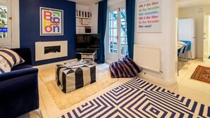 A living room with a fireplace, a television, a bookshelf, and a large window with curtains. - Host & Stay | Montpelier Colours (Brighton and Hove)