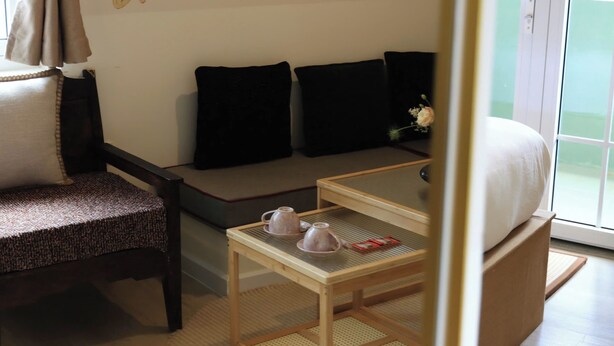 A hotel room with a sofa, a chair, a small table with a teapot and cups, and a bed. - Le Macaron Garden Stay - Boutique Hotel Da Lat (Cam Ly - Da Lat)