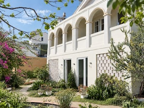 A building with a white facade, arched windows, and a garden with various plants and a water feature. - Le Macaron Garden Stay - Boutique Hotel Da Lat (Cam Ly - Da Lat)