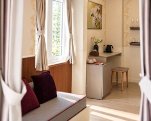 A cozy room with a sofa, a small table with a vase and a kettle, and a window with curtains. - Le Macaron Garden Stay - Boutique Hotel Da Lat (Cam Ly - Da Lat)