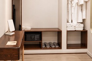 Habitación de hotel con escritorio de madera, microondas, zapatero y perchero con toallas dobladas.