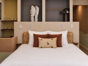 Habitación de hotel con una cama, dos mesitas de noche, un armario y un estante con artículos de aseo.