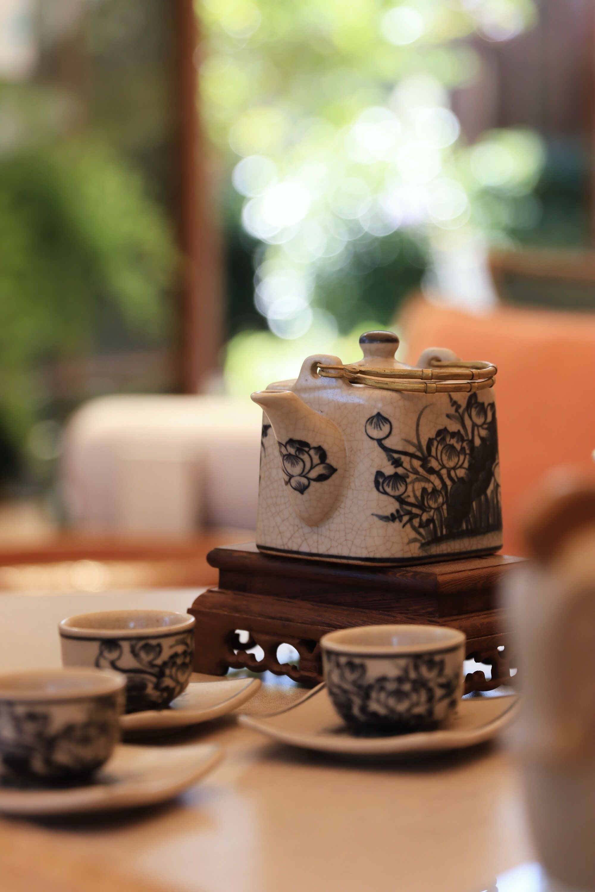 Une théière ornée de motifs floraux, posée sur un présentoir en bois, accompagnée de tasses et de soucoupes assorties, le tout disposé sur une table.
