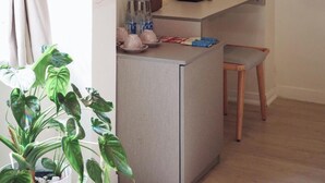 A small kitchenette with a coffee maker, a bottle of water, and a tissue box. There is a chair and a potted plant in the foreground. - Le Macaron Garden Stay - Boutique Hotel Da Lat (Cam Ly - Da Lat)