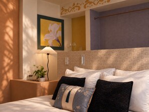 A hotel room with a bed, a nightstand with a lamp, a potted plant, and a wall-mounted artwork. - Le Macaron Garden Stay - Boutique Hotel Da Lat (Cam Ly - Da Lat)