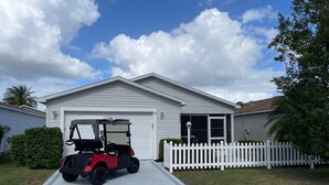 Ein Wohnhaus mit weißem Zaun, einer Auffahrt und einem roten Golfwagen, der davor geparkt ist.
