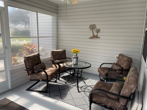 Relax in this serene sunroom with a glass door leading to the garden, a round table, and comfortable seating for four.